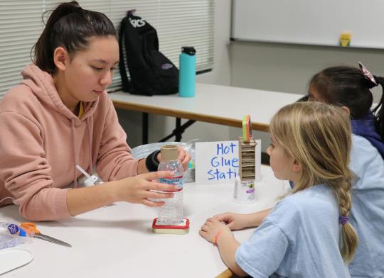 Student helping glue the recycle bots for children